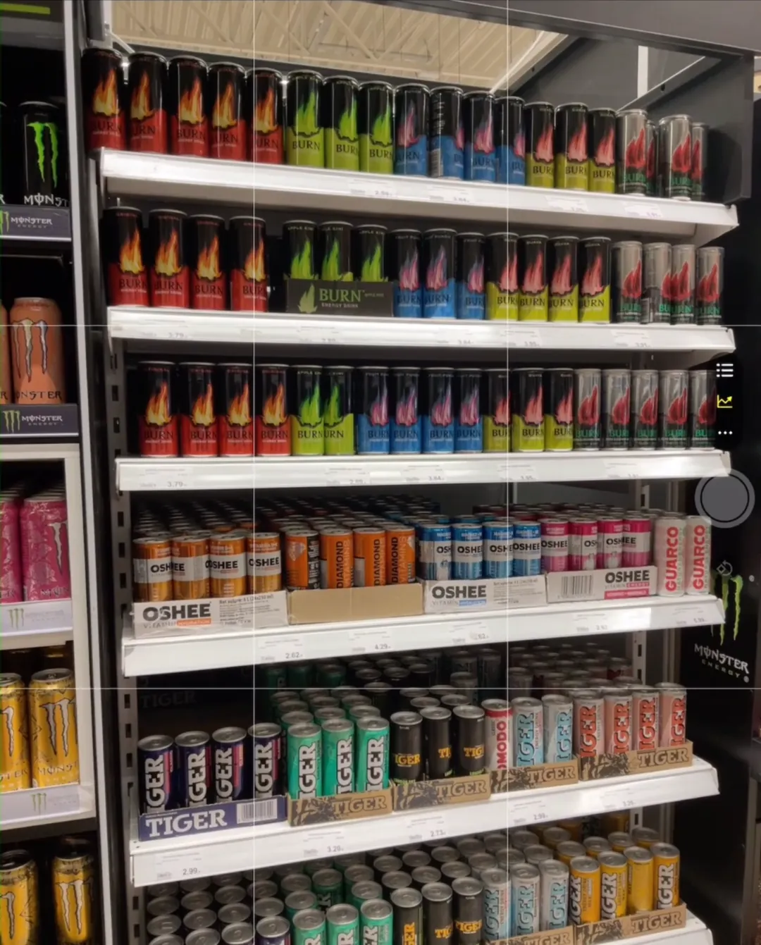 Ein Energydrink-Regal, mit der Asseco Platform Mobile App aufgenommen, mit Facings von Burn, Monster, Oshee, Tiger, Diamond, Guarco und Komodo auf sechs Regalböden