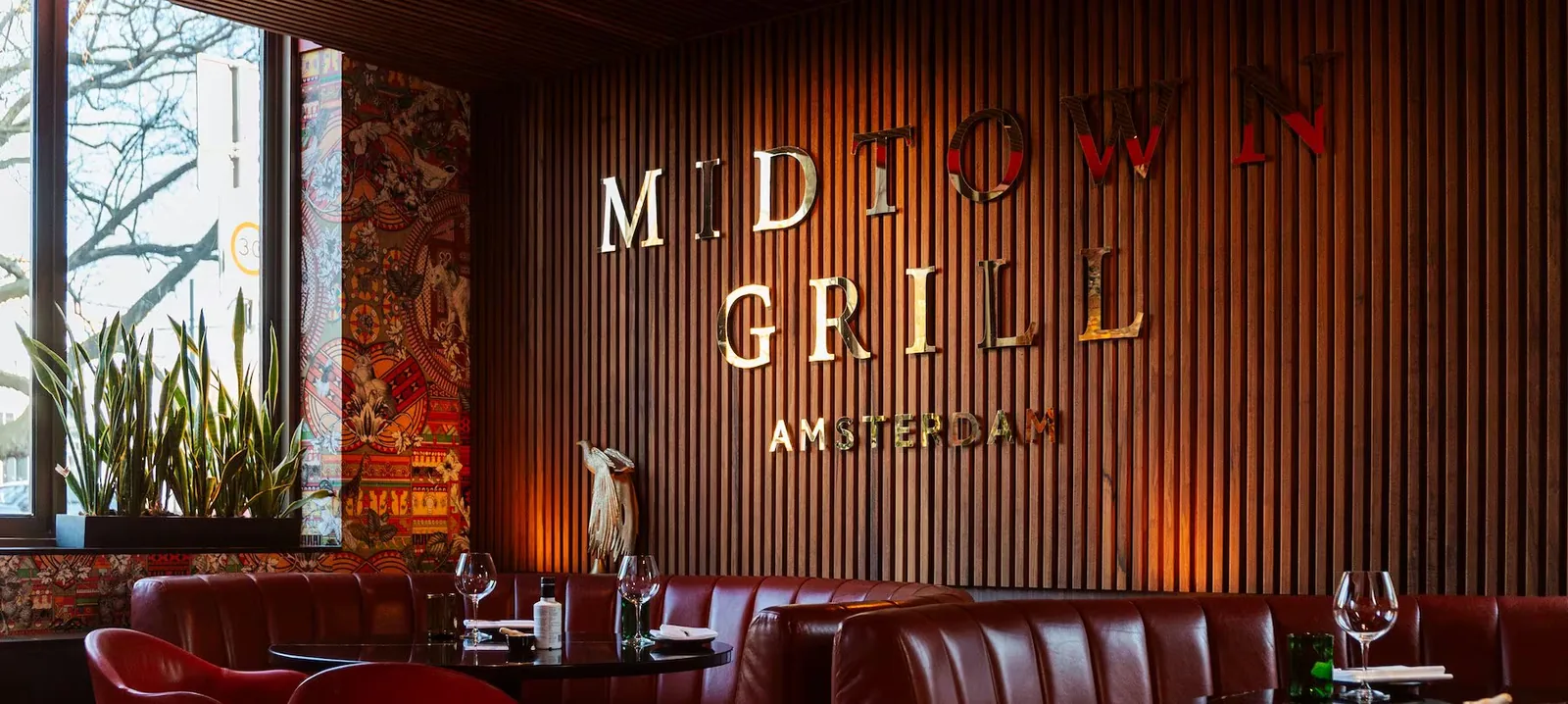 Innenraum des Restaurants Midtown Grill in Amsterdam, der Name in Metallbuchstaben auf einer Wand aus Holzlatten, darunter rote Lederbänke
