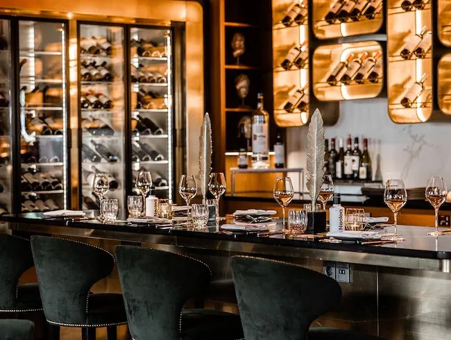 An der Bartheke ist für den Abend gedeckt, dahinter eine beleuchtete Wand mit Weinflaschen im Midtown Grill in Amsterdam
